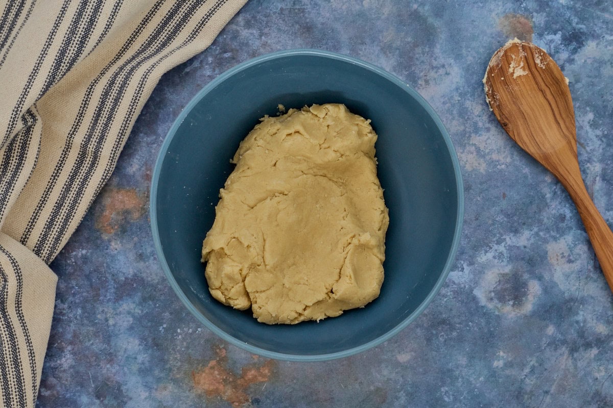 dough in a mixing bowl with a kitchen towel and wooden spoon alongside