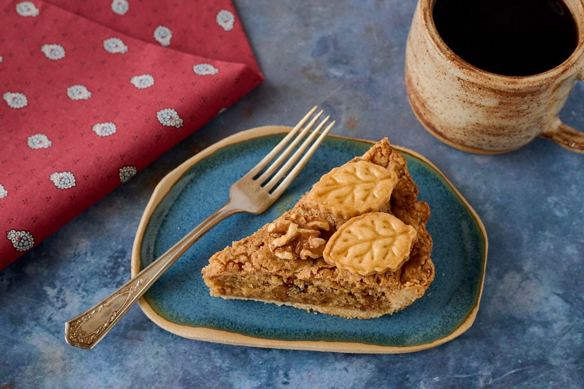 a slice of tart on a plate with a fork and a napkin and cup of coffee
