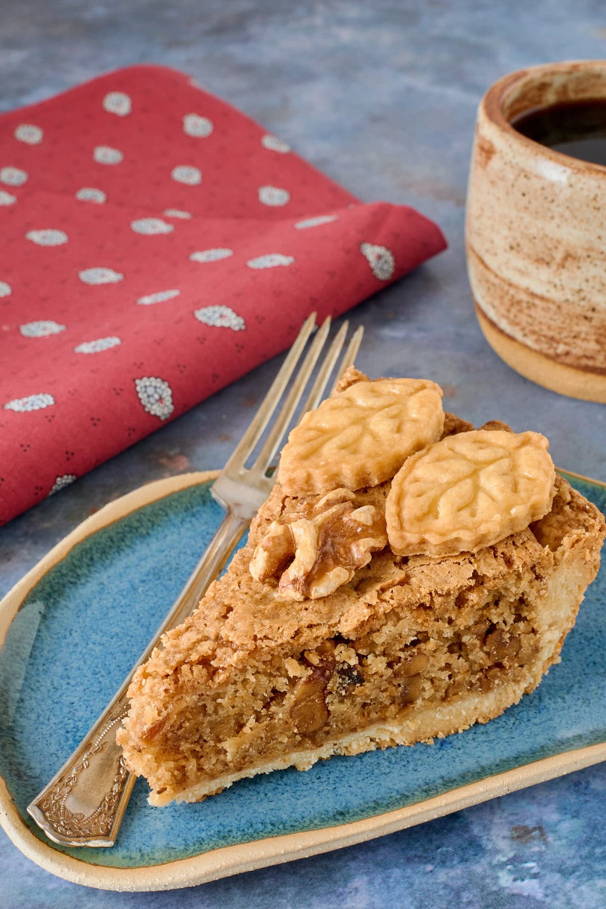 a slice of tart on a plate with a fork, napkin, and ceramic cup