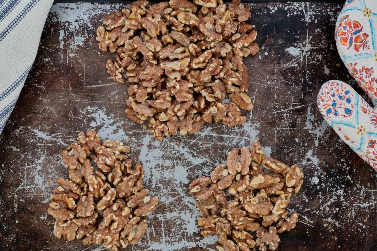 three groupings of walnuts on a cutting board with a kitchen towel and oven mitt