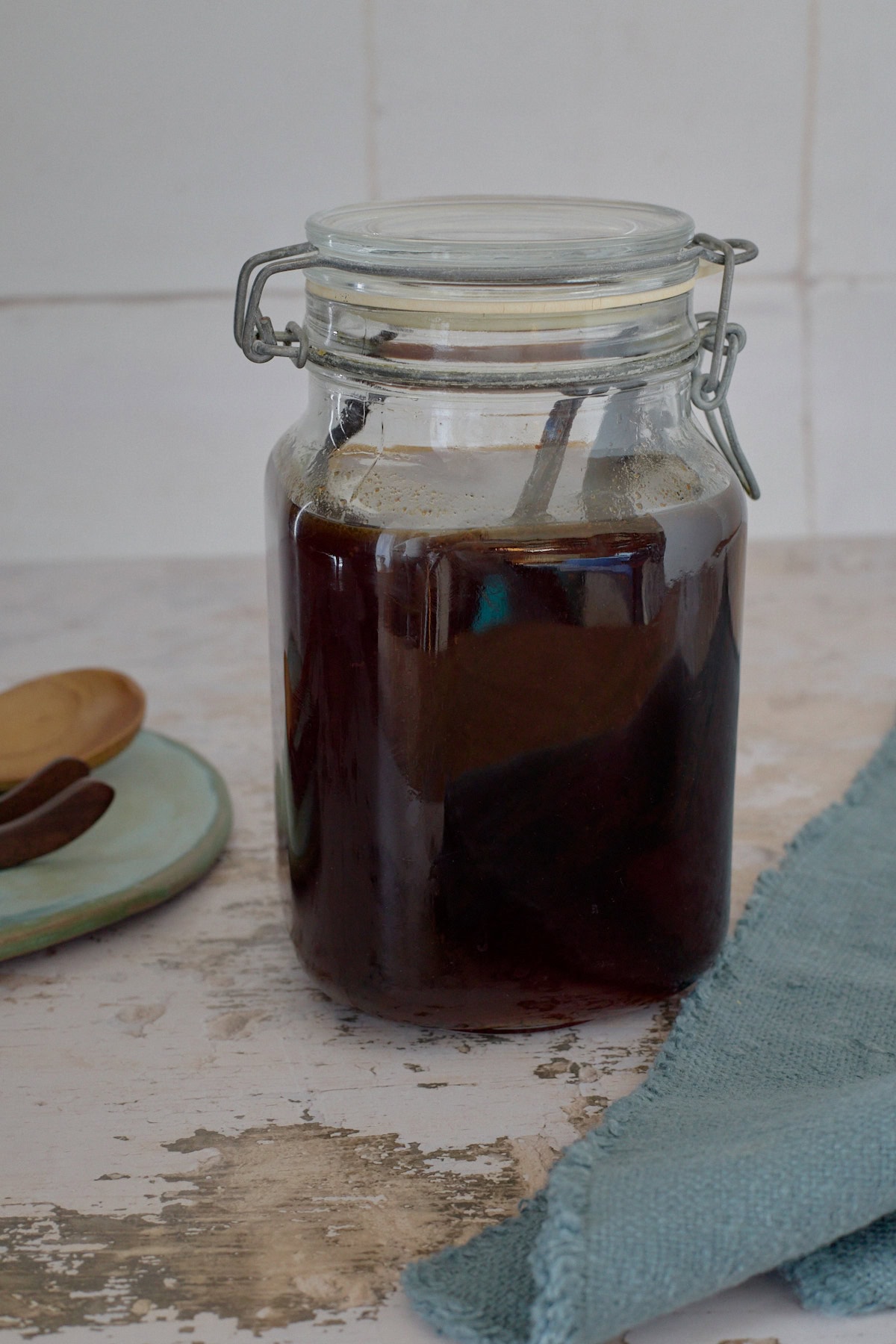 a jar of liqueur with vanilla beans, a plate with wooden tongs and a wooden spoon, and a napkin