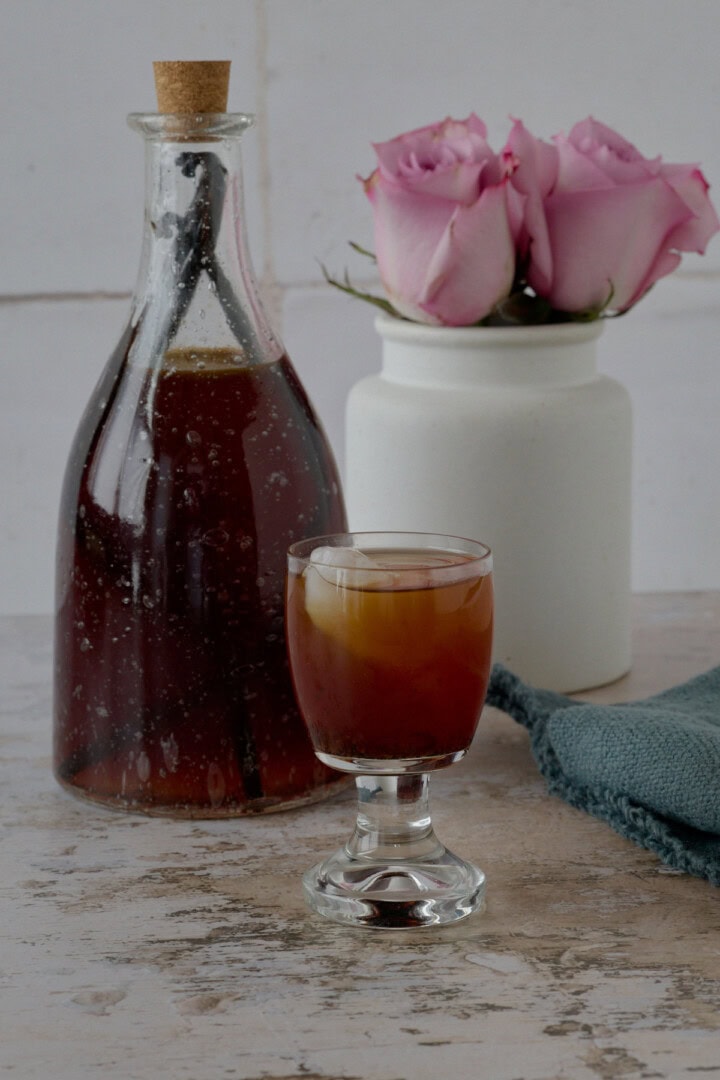 a bottle and glass of liqueur, vase of roses, and a napkin