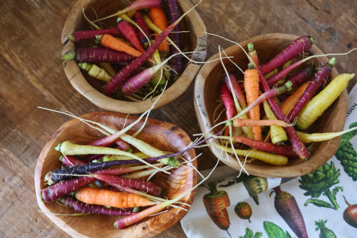 heirloom carrots in wood bowls with a kitchen towel alongside