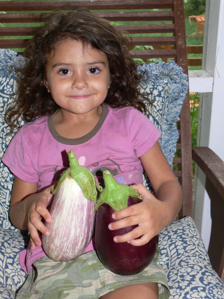 a young girl in a chair holding 2 eggplants