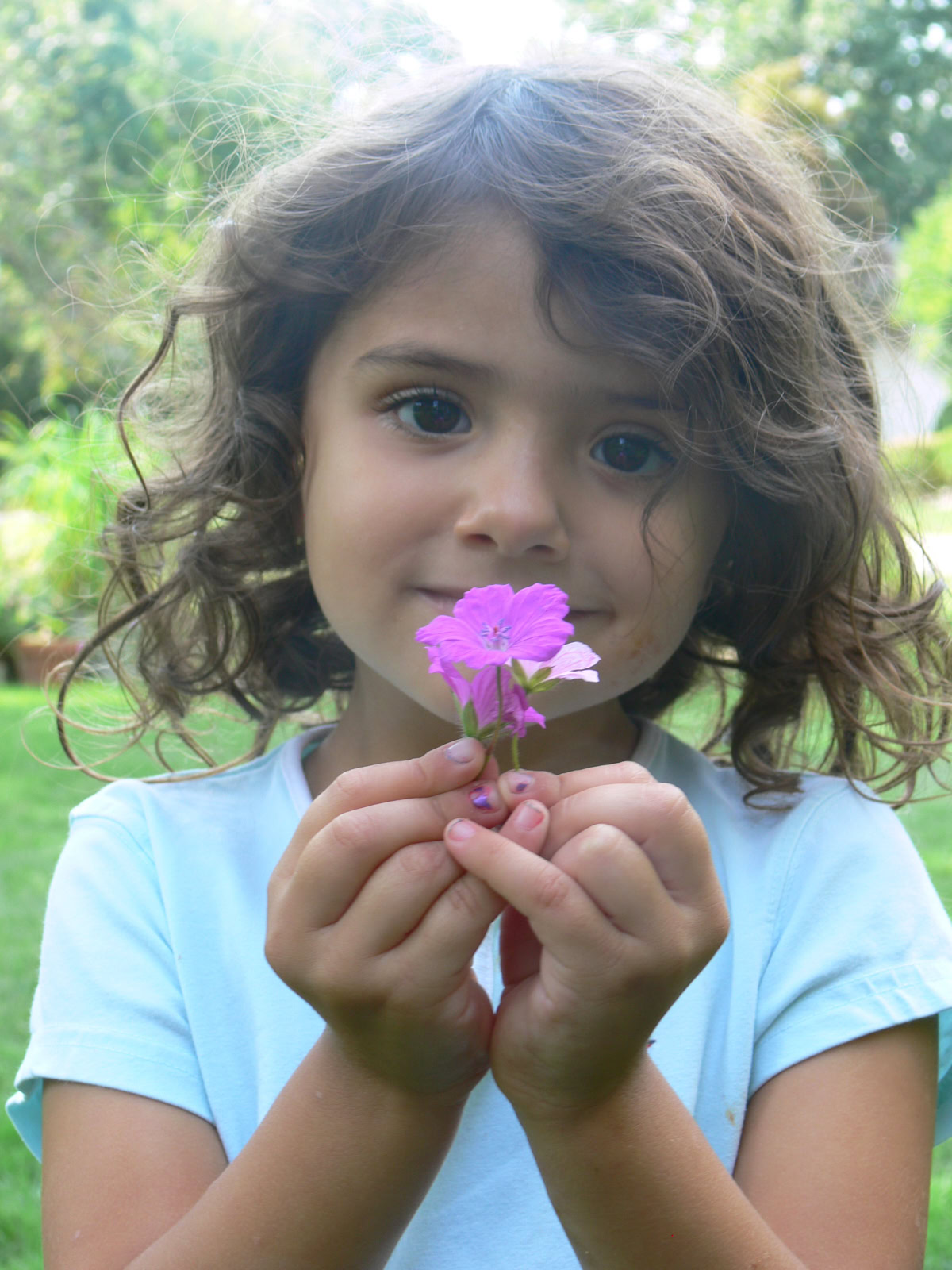 a young girl standing outside, holding hardy geranium flowers