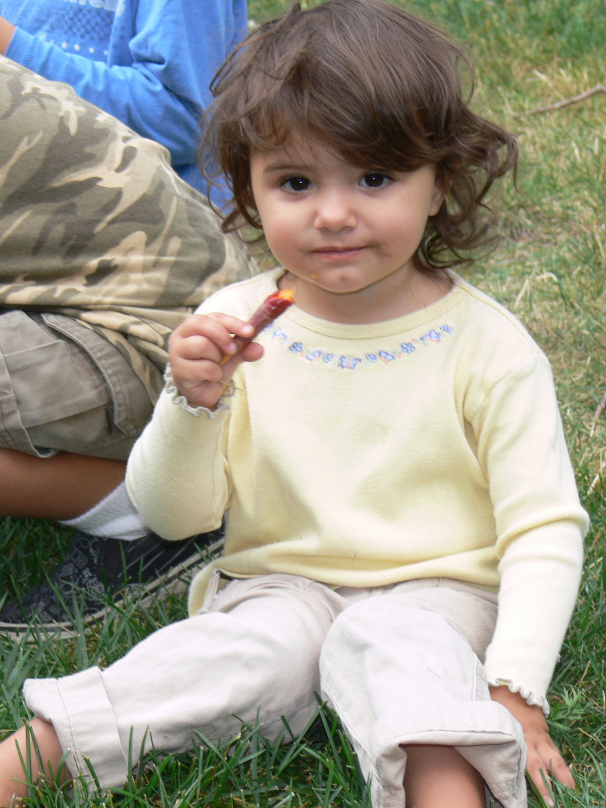 a young girl sitting on the grass, eating a freshly-picked carrot