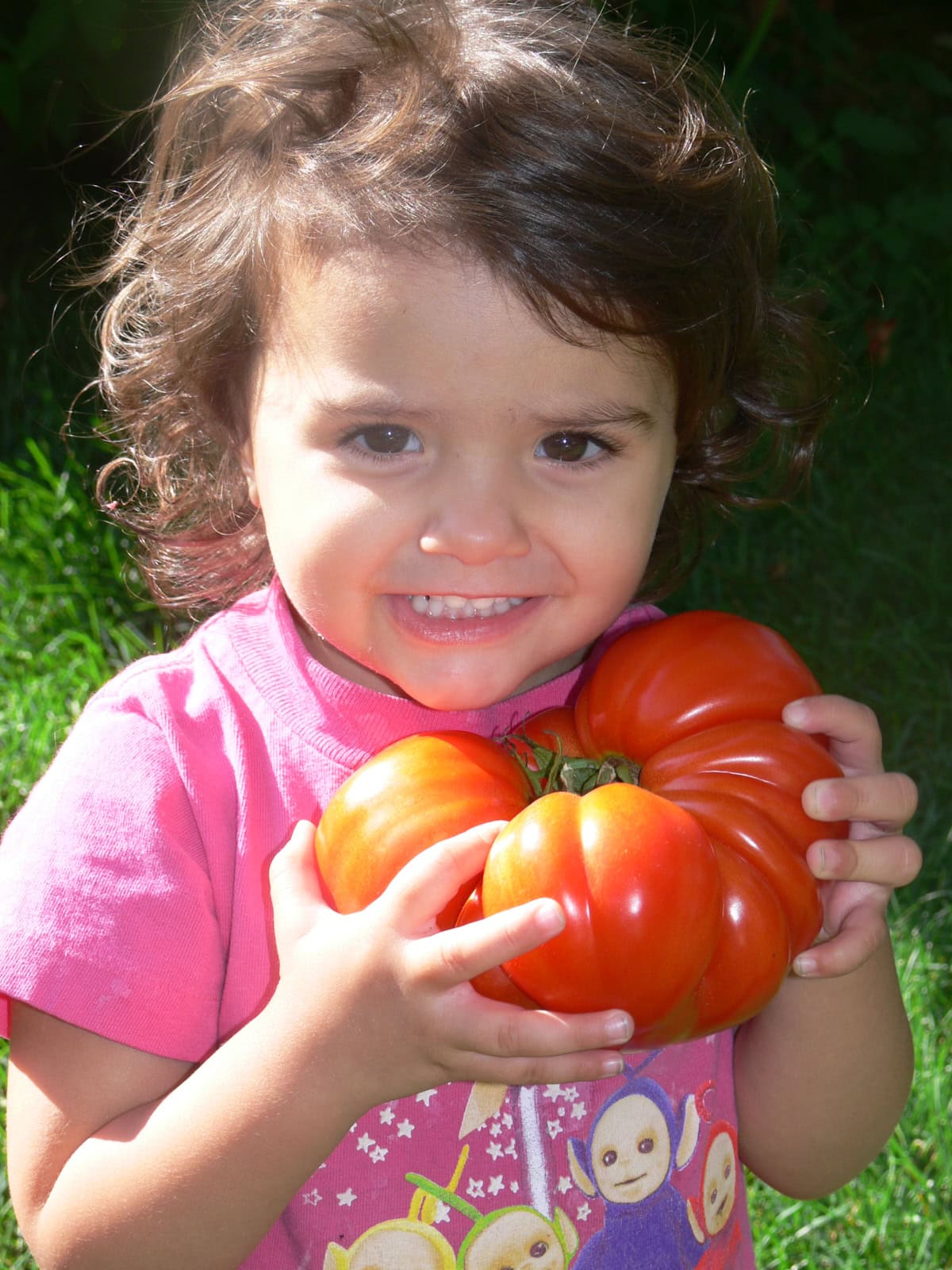 a young girl holding a large red tomato