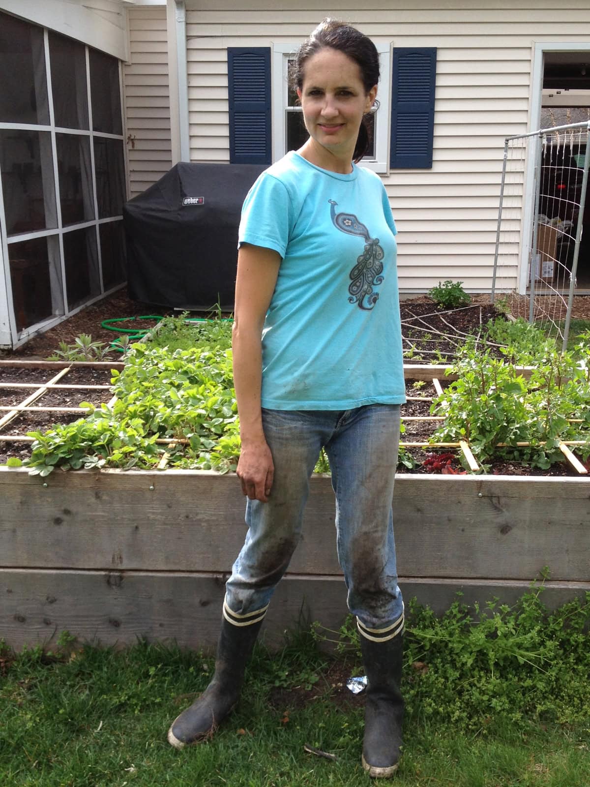 a woman in dirty gardening clothes standing in front of raised bed gardens