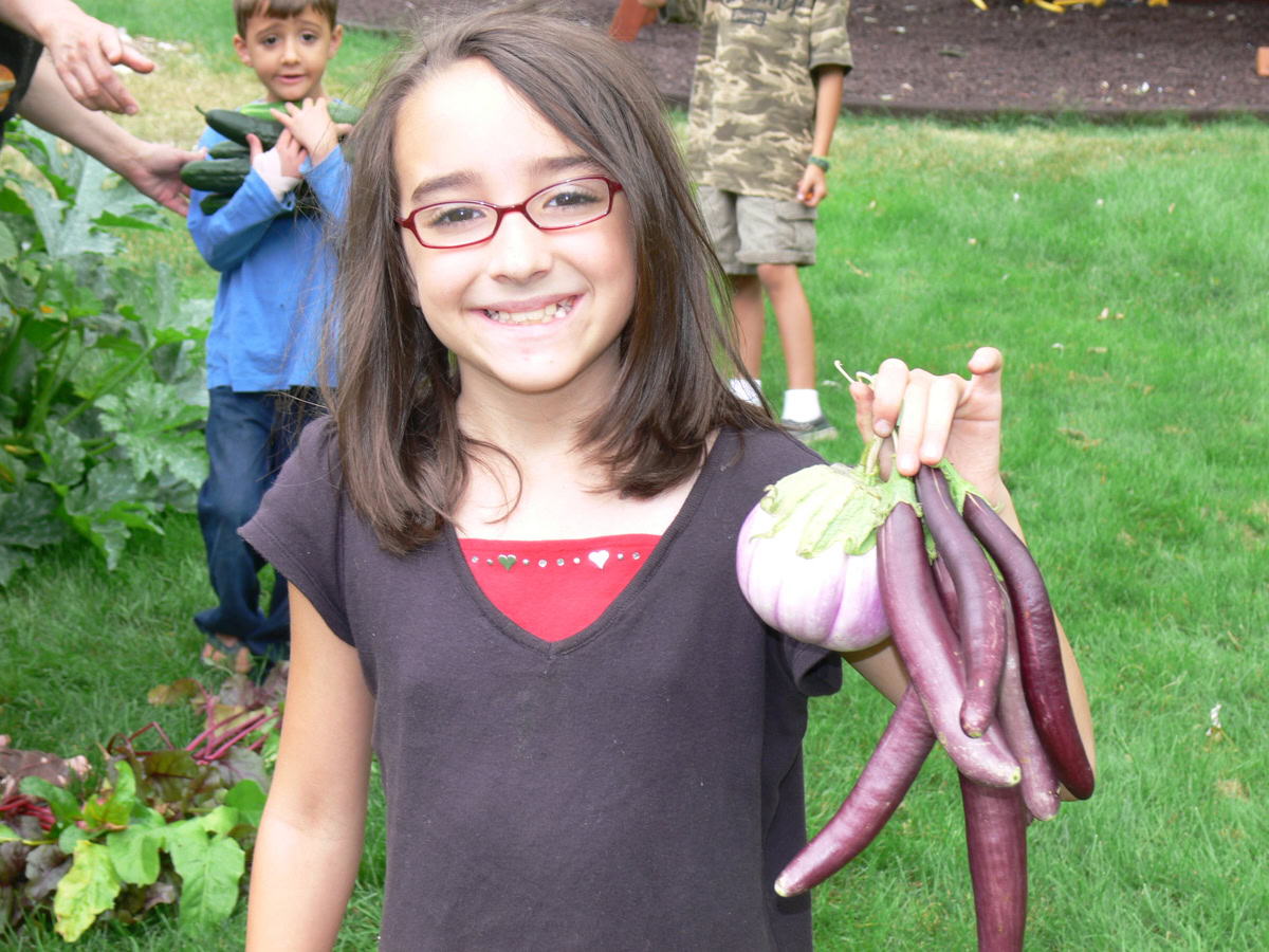 a girl holding eggplants and a boy holding cucumbers