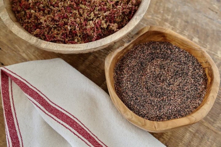 amaranth seeds and flowers in wooden bowls with a kitchen towel in the foreground