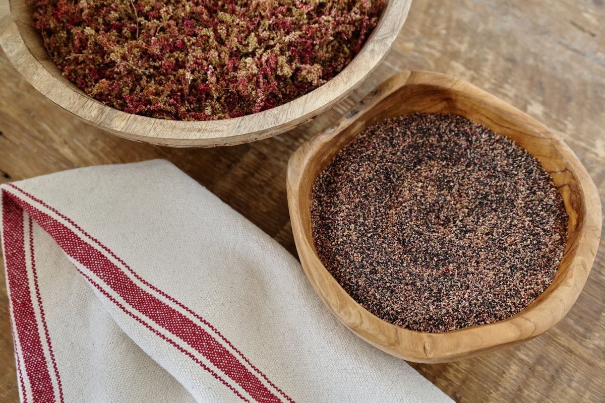 amaranth seeds and flowers in wooden bowls with a kitchen towel in the foreground