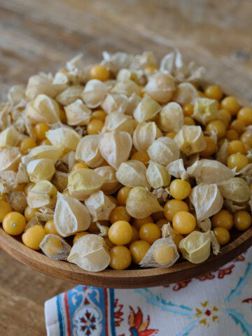 freshly-picked ground cherries in a wooden bowl with a kitchen towel in the foreground