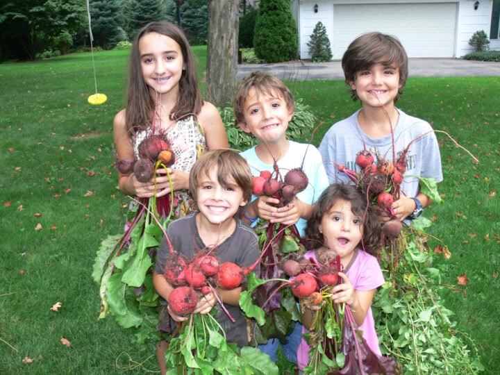 5 kids standing outside on the grass, holding freshly dug beets from the garden