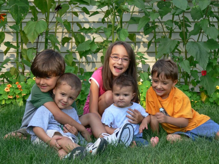 5 young kids sitting in the grass in front of some nasturtiums and sunflowers