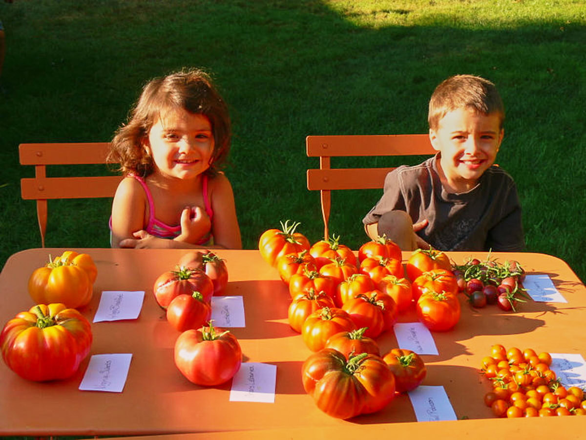 a young boy and young girl sitting at an outdoor table with labeled heirloom tomatoes on it