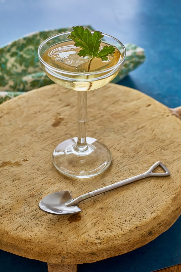 liqueur in a glass with ice and a fresh leaf, a napkin, a wood tray, and a shovel-shaped spoon