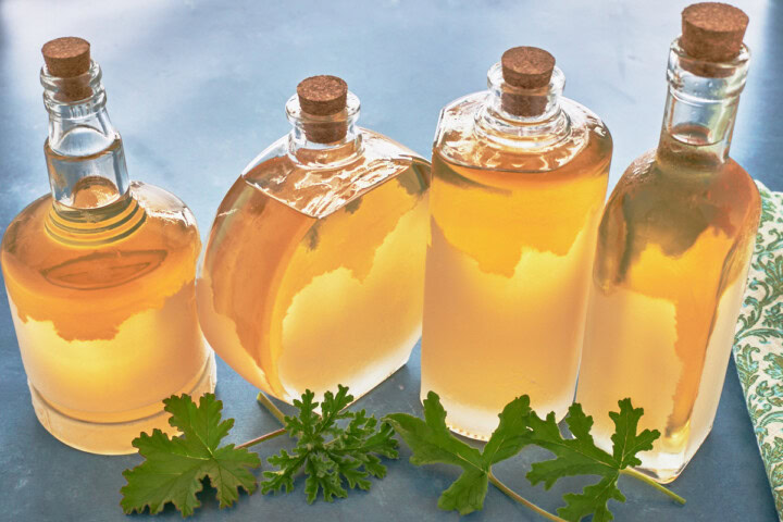 4 glass bottles with liqueur and corks with scented geranium leaves in front and a napkin alongside