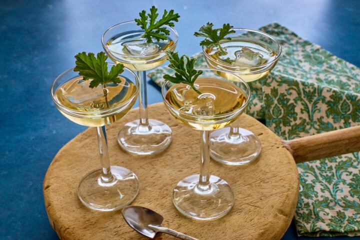 liqueur in 4 glasses with ice and a fresh leaf in each on a wood tray with a shovel-shaped spoon and a napkin in the background