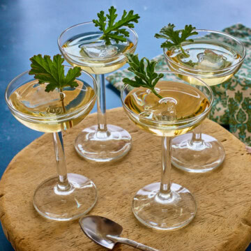 liqueur in 4 glasses with ice and a fresh leaf in each on a wood tray with a shovel-shaped spoon and a napkin in the background
