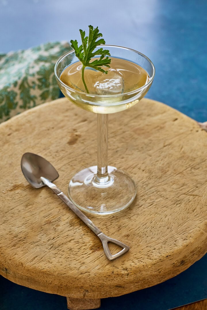 liqueur in a glass with ice and a fresh leaf, a napkin, a wood tray, and a shovel-shaped spoon