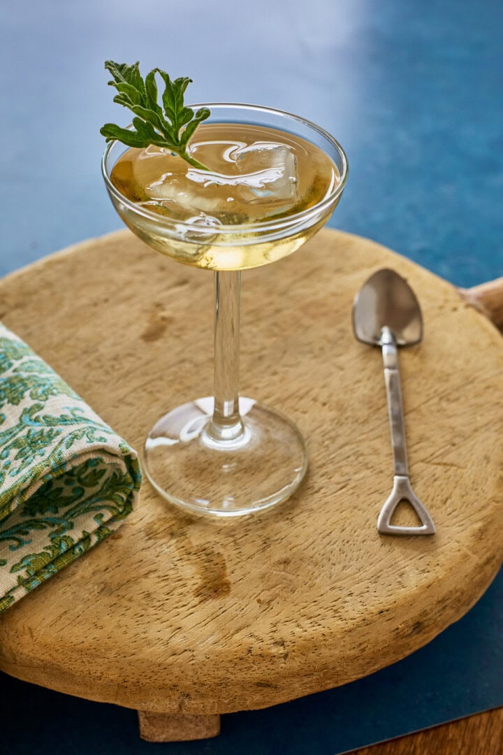 liqueur in a glass with ice and a fresh leaf, a napkin, a wood tray, and a shovel-shaped spoon