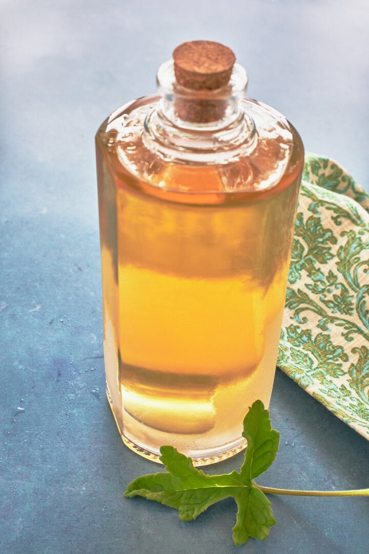 rober's lemon rose scented geranium liqueur in a bottle with a cork with a fresh leaf in front and a napkin alongside